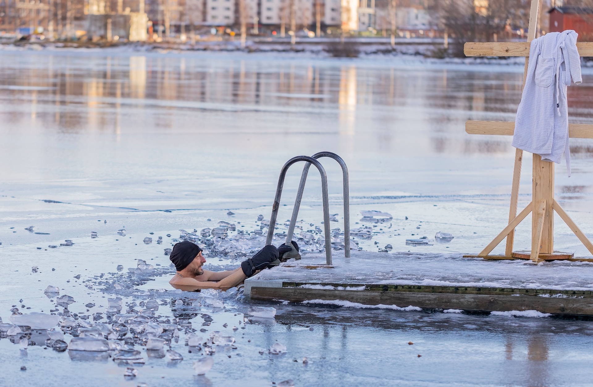 A man in a woolen cap resting in an ice bath cut into a frozen lake