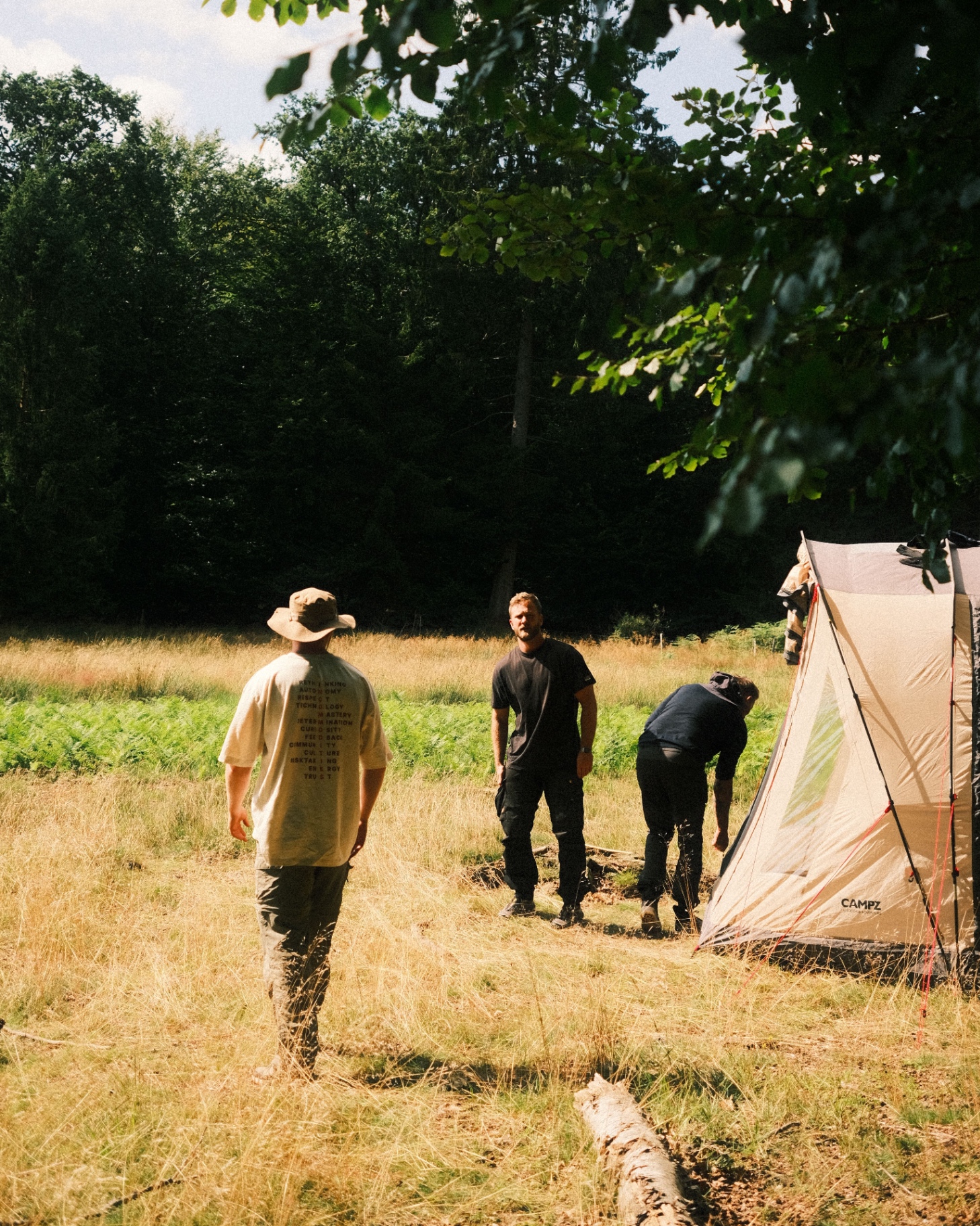 Men setting up a tent together in a sunlit meadow