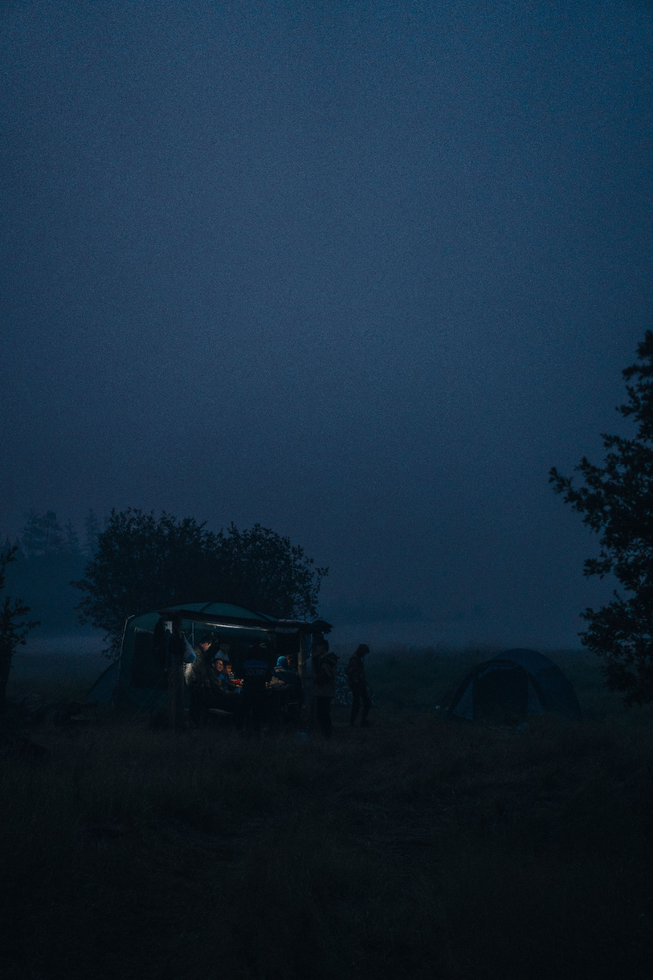 A lit camp gathering in the fog at nightfall